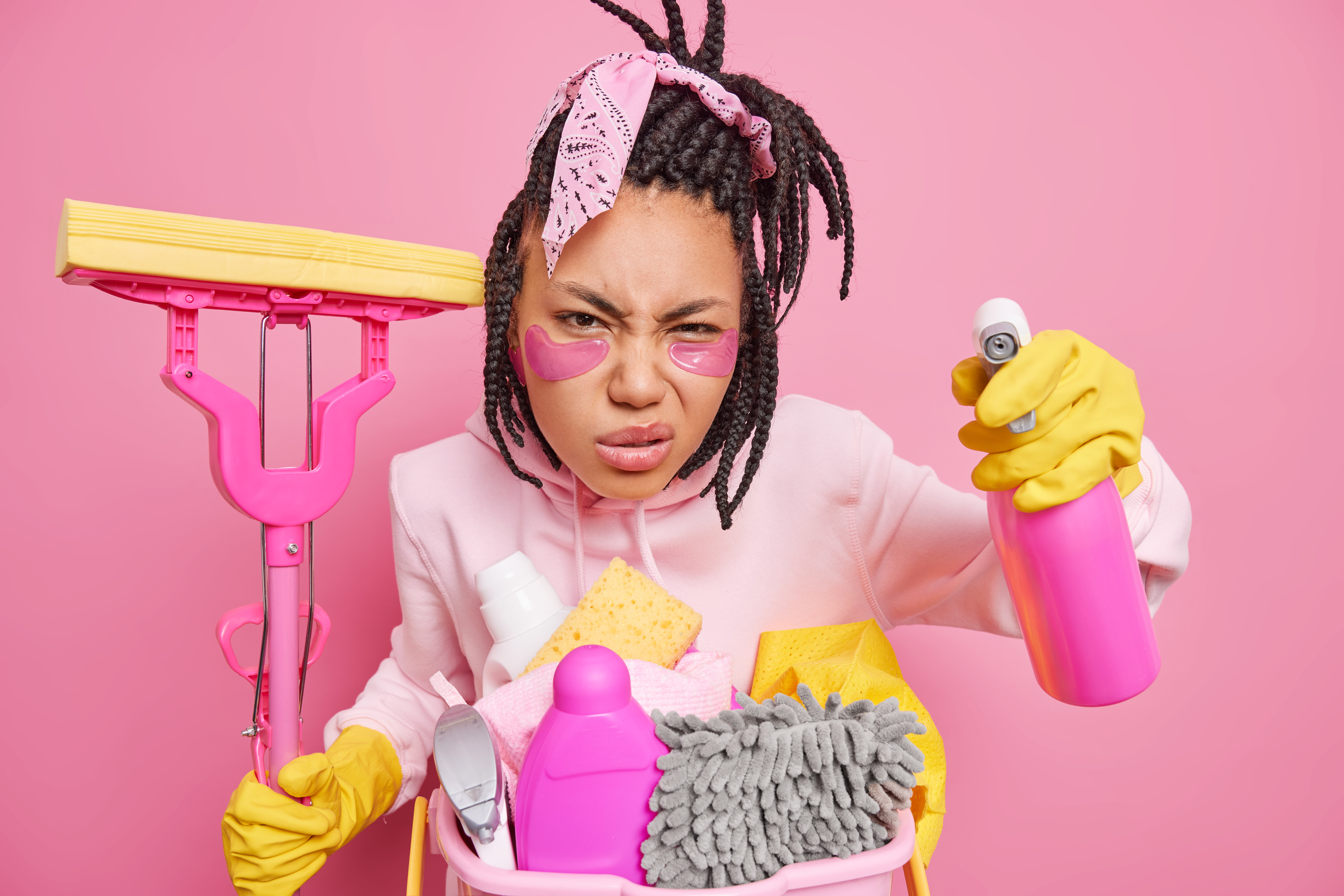 Photo of dissatisfied housewife poses with housecleaner tools cares about purity smirks face looks scrupulously at something dirty holds mop cleaning detergent isolated over pink background.